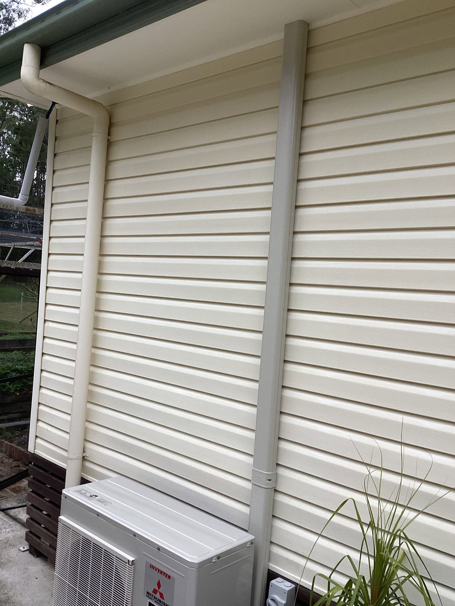 Mitsubishi air conditioning outdoor unit installed against cream vinyl siding