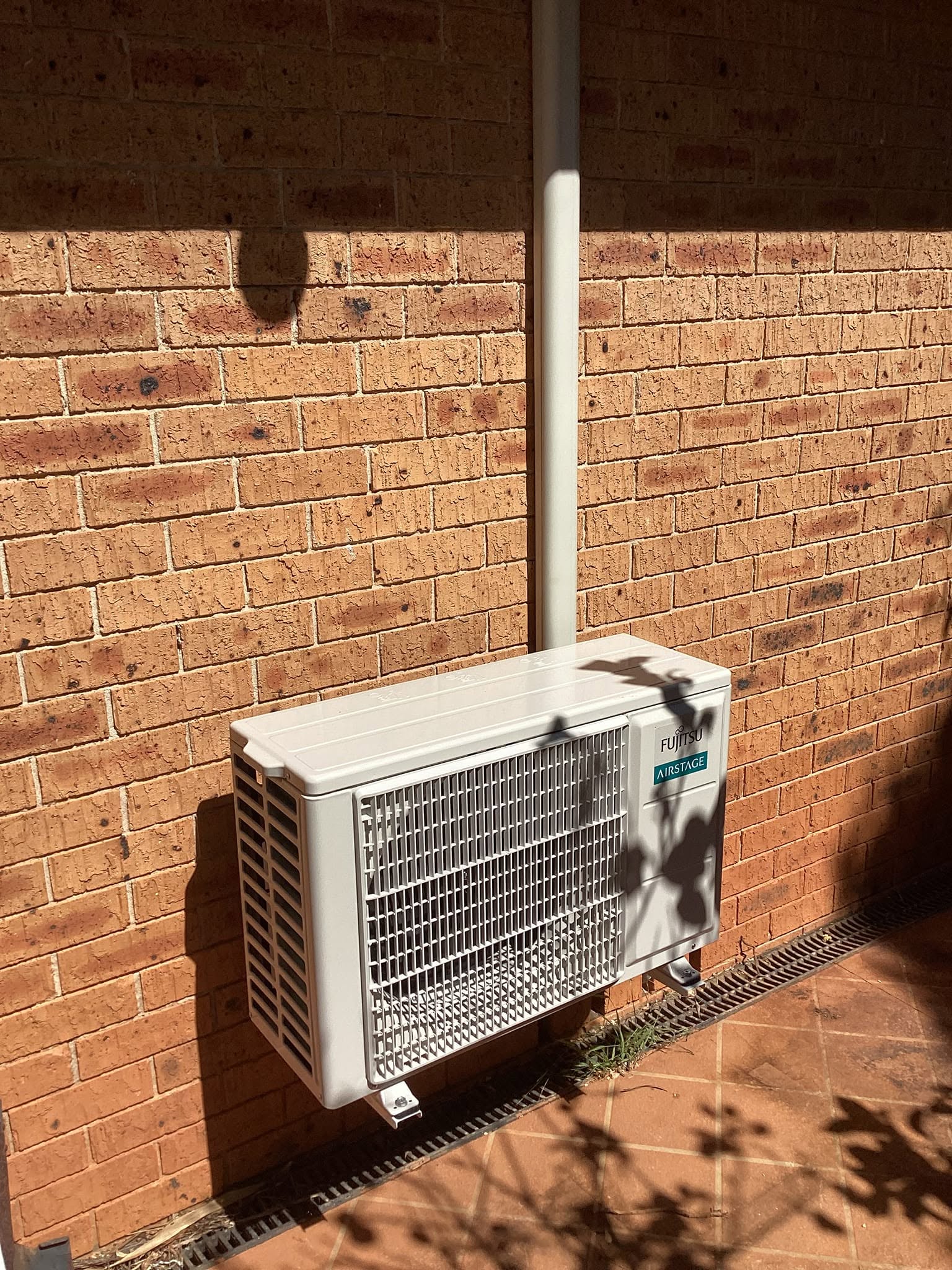 Fujitsu Airstage air conditioning condenser unit professionally installed on a brick exterior wall